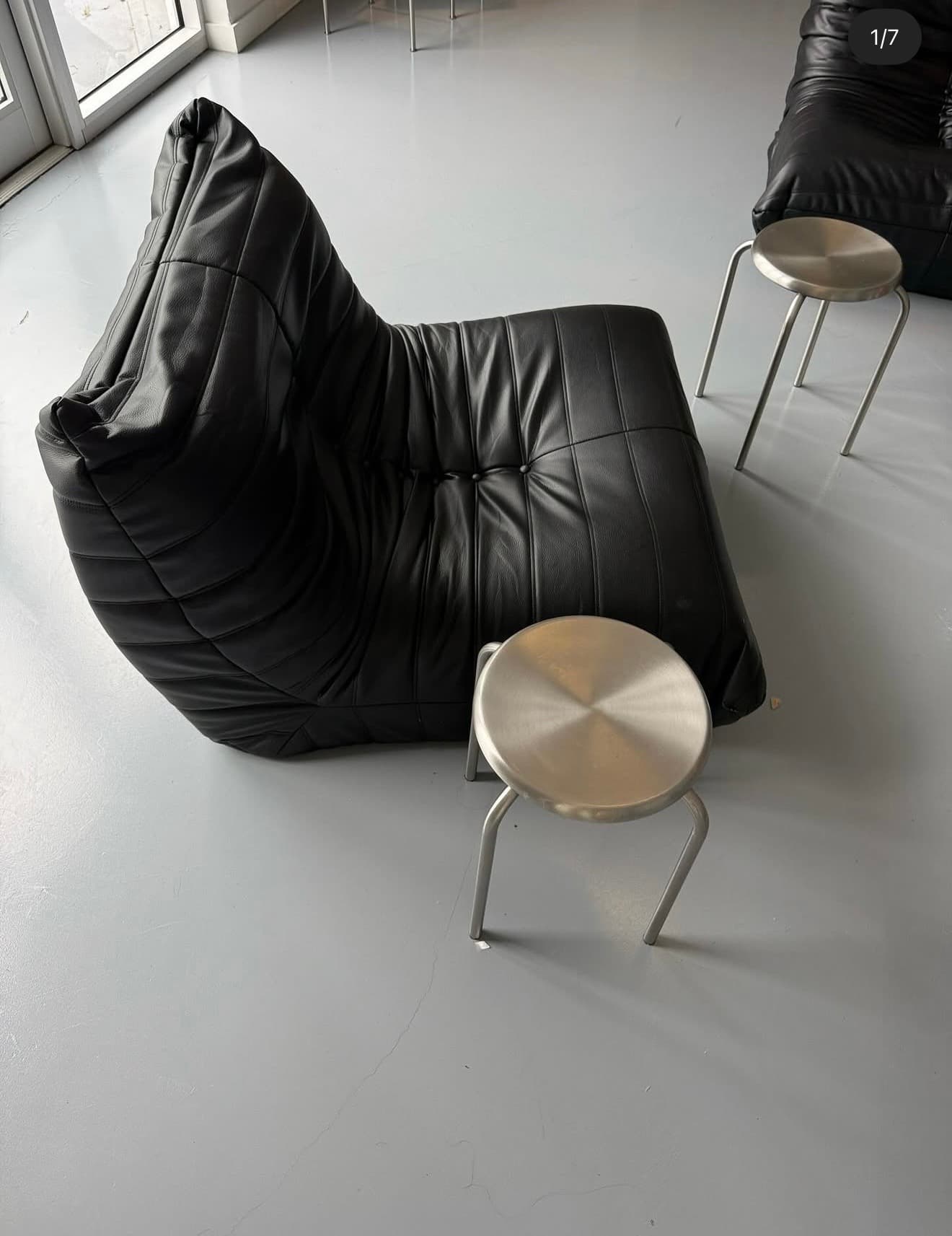 Sculptural black leather lounge chair paired with brushed metal stools