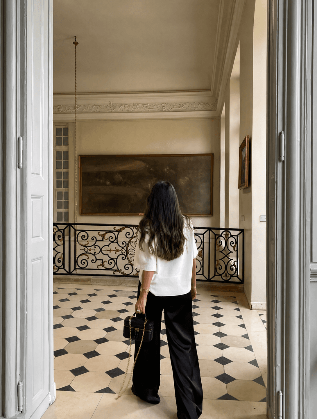 A woman in a white top and black trousers standing within an elegant architectural interior